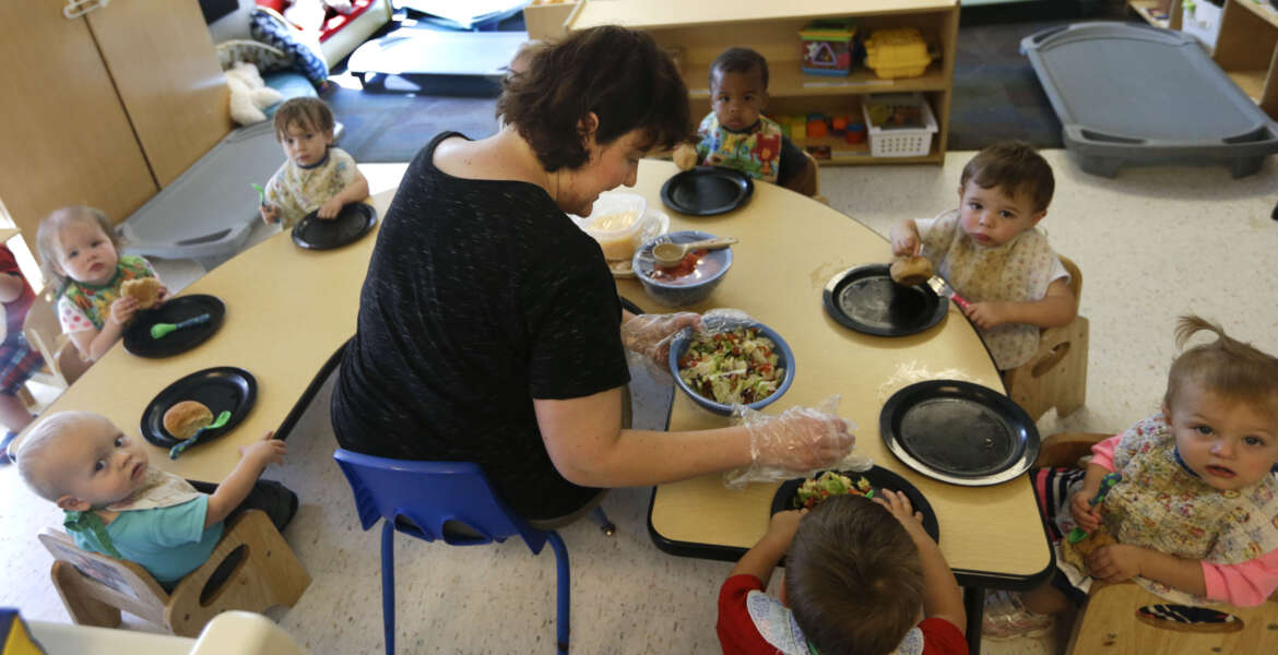 Alyssa Breitmayer feeds her class of one-year-olds at the Olathe Family YMCA in Olathe, Kan., Wednesday, June 24, 2015. As early childhood teachers lament toddlers too large to fit in playground swings, officials are mulling changes designed to make meals served to millions of kids in day care healthier.  (AP Photo/Orlin Wagner)