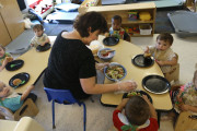 Alyssa Breitmayer feeds her class of one-year-olds at the Olathe Family YMCA in Olathe, Kan., Wednesday, June 24, 2015. As early childhood teachers lament toddlers too large to fit in playground swings, officials are mulling changes designed to make meals served to millions of kids in day care healthier.  (AP Photo/Orlin Wagner)