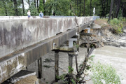 FILE- In this Monday, Oct. 5, 2015 file photo, Residents of a lakeside neighborhood walk across Overcreek Bridge by the remains of a failed dam in Columbia, S.C. Officials say the structure beneath a road collapsed Monday afternoon following days of heavy rain, nearly emptying a lake in a few minutes. No one was injured. South Carolina had problems with crumbling roads and bridges and old drinking water systems and dams long before the historic floods of the past week. Now the state faces what will likely be hundreds of millions if not billions of dollars of bills to fix washed out roads and bridges and destroyed dams. (AP Photo/Jay Reeves, File)