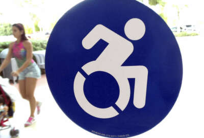 In this Wednesday, Oct. 7, 2015 photo, a modernized handicapped sign is affixed to a door at the The Mall at Millenia in Orlando, Fla. Advocates want to replace the familiar image of a stick figure in a wheelchair with this action-oriented logo to emphasize ability, not disability.  (AP Photo/Bill Sikes)