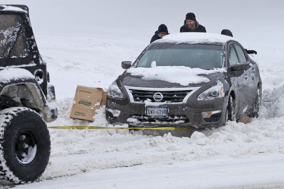 Passers-by help push a stuck car out of the snow as another motorist tows it out in Richmond, Va., Saturday, Jan. 23, 2016. A winter storm has hit the East Coast, creating a blizzard with brutally high winds, dangerous inland flooding and white-out conditions. (AP Photo/Steve Helber)