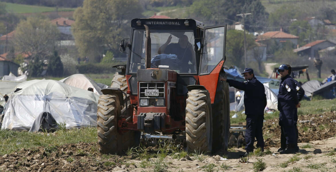 Greek police officers speak with Lazaros Oulis, farmer and owner of fields near the makeshift refugee camp at the northern Greek border point of Idomeni, Greece, Thursday, March 31, 2016. Oulis, tried to plough his land on Thursday, driving the tractor near the  tents and people.(AP Photo/Darko Vojinovic)