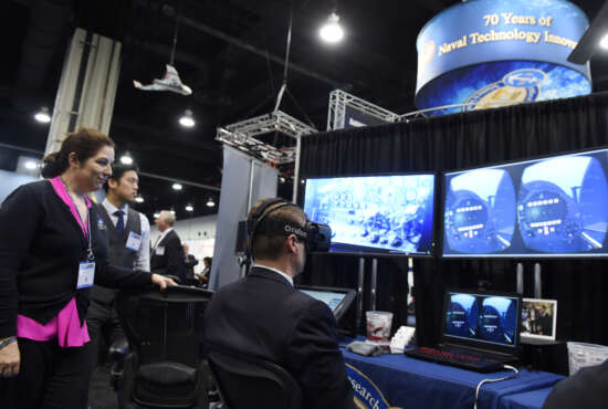 NATIONAL HARBOR, Md. (May 16, 2016) Lauren Burnette, from Space and Naval Warfare Systems Command (SPAWAR) Systems Center Pacific, explains the Battlespace Exploitation of Mixed Reality (BEMR) Lab demo to a visitor at the Office of Naval Research (ONR) exhibit during the 2016 Sea-Air-Space Exposition. BEMR is designed to showcase and demonstrate cutting edge low cost commercial mixed reality, virtual reality and augmented reality technologies and to provide a facility where warfighters, researchers, government, industry and academia can collaborate. (U.S. Navy photo by John F. Williams/Released) 