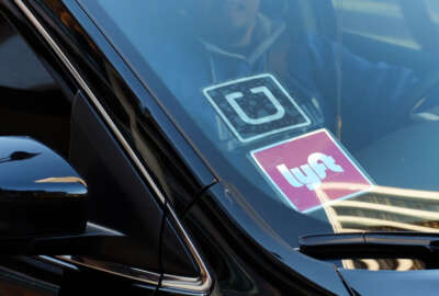 FILE - In this Tuesday, Jan. 12, 2016, file photo, a driver displaying Lyft and Uber stickers on his front windshield drops off a customer in downtown Los Angeles. Hailing a ride with a smartphone app in many U.S. cities could come down to a fight over fingerprints. Following incidents where Uber drivers were found to have criminal records, a growing number of state and local governments want ride-hailing drivers to undergo fingerprint background checks. Uber and its chief rival, Lyft, have fought those checks, contending their own method of vetting drivers is just as safe. (AP Photo/Richard Vogel, File)
