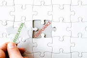 Hand with missing jigsaw puzzle piece. Word REGULATION, covering  text COMPLIANCE. Business concept image for completing the final puzzle piece.