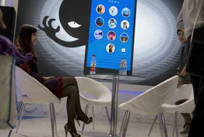 In this April 29, 2016, file photo, a woman sits near a display showing the dangers of hackers breaking into mobile devices during the Global Mobile Internet Conference in Beijing. Chinese electronics maker Hangzhou Xiongmai Technology has issued a recall on Monday, Oct 24, 2016, for millions of products sold in the U.S. following a devastating cyberattack, but has lashed out at critics who say its devices were at fault.  (AP Photo/Ng Han Guan, File)