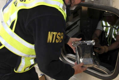 In this photo released by the National Transportation Safety Board (NTSB), James Southworth, Investigator-in-Charge for the National Transportation Safety Board’s investigation, is handed the lead car’s video recorder in an anti-static bag from NTSB investigator Michael Hiller, Tuesday, Oct. 4, 2016, in Hobokon, N.J. Federal investigators recovered a data recorder, video recorder and the engineer's cellphone Tuesday from the commuter train that crashed into a New Jersey rail station last week. The items were sent to an agency lab for analysis.  (N.J. Transit Police Det. Laquan Hudson/NTSB via AP)
