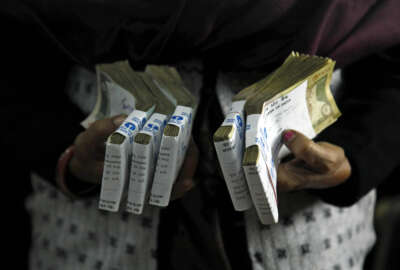 FILE - In this Dec. 16, 2011 file photo, a cashier holds bundles of Indian rupee bank notes at a bank in Allahabad, India. India's prime minister has announced late Tuesday, Nov. 8, 2016, scrapping of high denomination 500 and 1,000 Indian rupees currency notes in what he describes as a major step to fight the menace of black money, corruption and fake currency. Prime Minister Narendra Modi in a speech carried live on radio and television on Tuesday says there is no need to panic as people would be able to deposit these currency notes in their bank account until December 30. (AP Photo/Rajesh Kumar Singh, File)