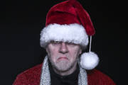 Bearded middle aged grumpy man in  Father Christmas fancy dress with Christmas hat and coat.