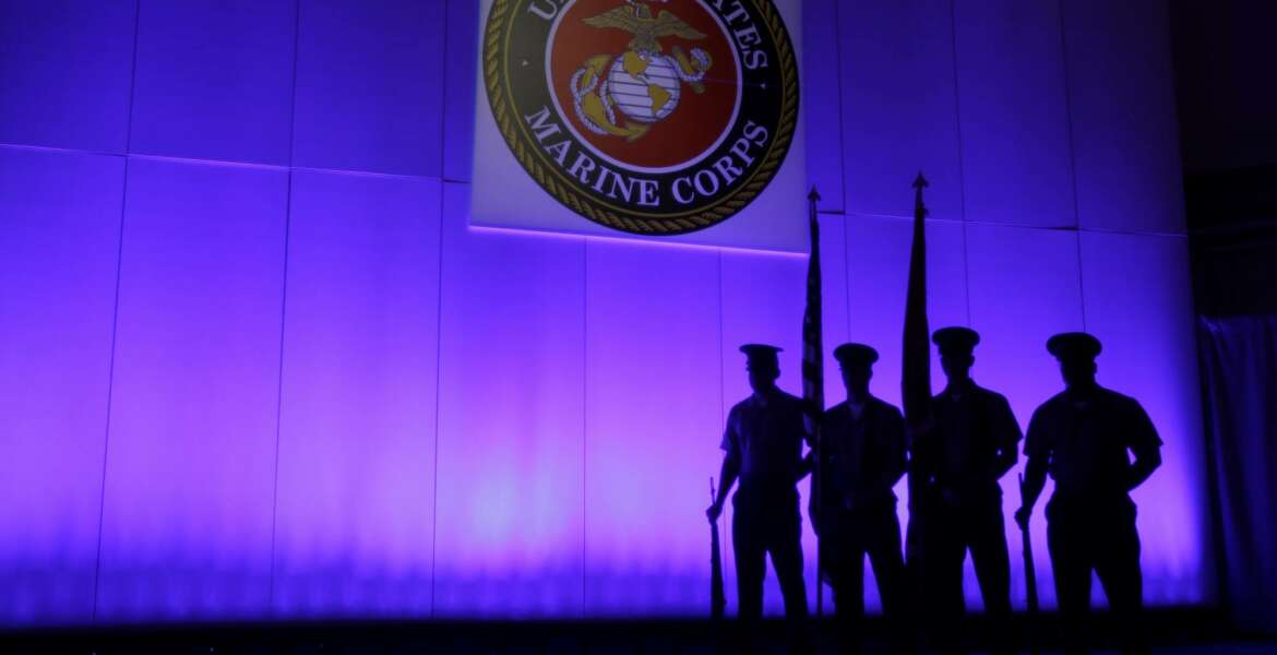FILE- In this May 5, 2014, file photo, a U.S. Marine Corps Color Guard stands under a Marine Corps emblem in Jupiter, Fla. The Defense Department is investigating reports that some Marines shared naked photographs of female Marines, veterans and other women on a secret Facebook page, some of which were taken without their knowledge. Marine Corps Commandant Gen. Robert B. Neller on Sunday, March 5, 2017, called the online activity 