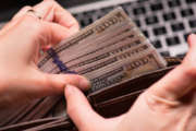 Close up of female hands counting US dollar banknotes at the table in front a laptop computer. Woman accountant with money and notebook.