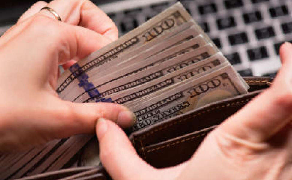 Close up of female hands counting US dollar banknotes at the table in front a laptop computer. Woman accountant with money and notebook.