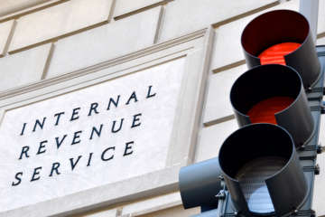 Internal Revenue Service sign with a traffic signal in the foreground indicating a red light.