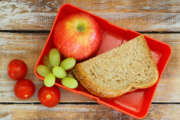 Lunch box with brown bread sandwich, red apple, grapes and cherry tomatoes