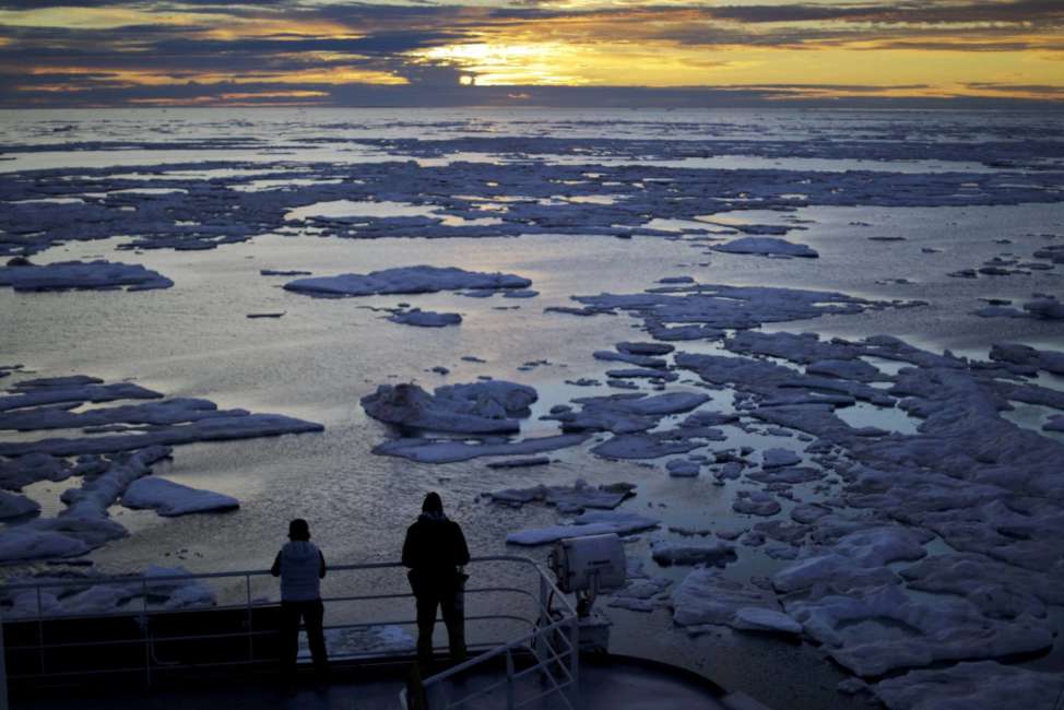 FILE - In this July 21, 2017 file photo, researchers look out from the Finnish icebreaker MSV Nordica as the sun sets over sea ice floating on the Victoria Strait along the Northwest Passage in the Canadian Arctic Archipelago. Studies show the Arctic is heating up twice as fast as the rest of the planet. Scientists are concerned because impacts of a warming Arctic may be felt elsewhere. (AP Photo/David Goldman, File)