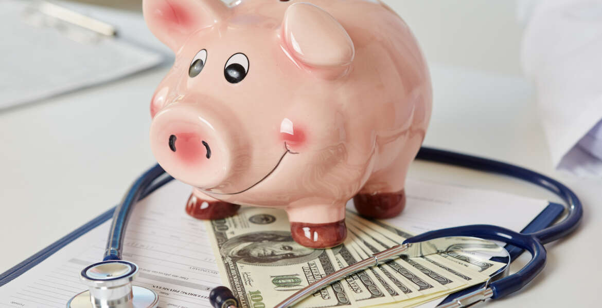Funny piggybank standing on clipboard with document, bunch of hundred dollar banknotes and stethoscope closeup. Medical service economy, health care savings and insurance concept. Focus on piggy bank