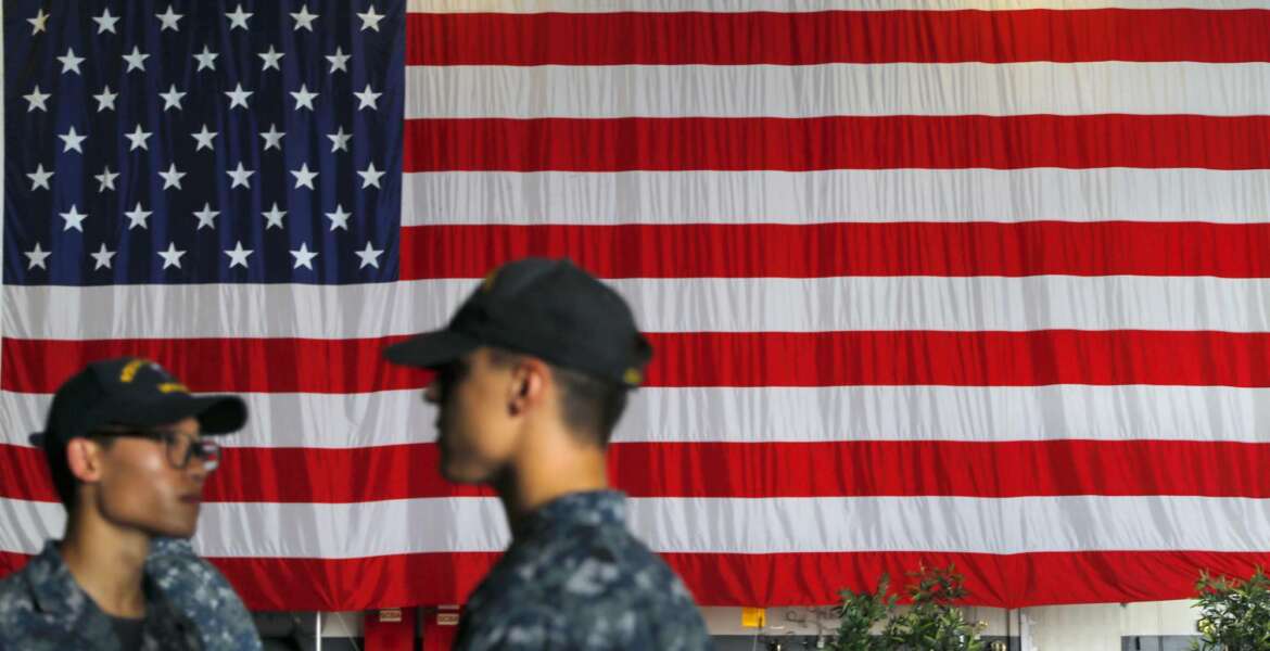 U.S. Navy servicemen stand in front of an American national flag at the USS Ronald Reagan aircraft carrier in Hong Kong, Monday, Oct. 2, 2017. A senior U.S. Navy commander of the nuclear powered aircraft carrier reportedly participating in joint drills with South Korea later this month told reporters during a stop in Hong Kong on Monday that his strike group is committed to defending U.S. allies in the region. (AP Photo/Vincent Yu)