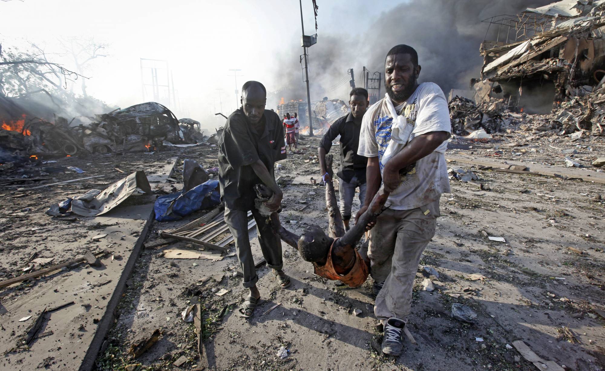 FILE - In this Oct. 14, 2017, file photo, Somalis remove the body of a man killed in a huge explosion blast in the capital Mogadishu, Somalia. Countless members of Somalia's vast diaspora have returned to Somalia in recent years to help rebuild their homeland after decades of civil war. Some who spoke to The Associated Press say they won't be deterred by the Oct. 14 bombing that killed more than 300. Instead, they say the attack marks a turning point, and is a call for all Somalis to work toward peace. (AP Photo/Farah Abdi Warsameh, File)