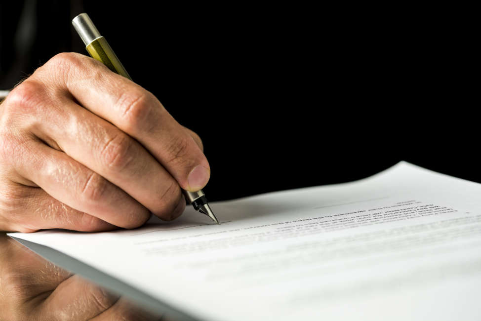 Closeup of male hand signing a contract, employment papers, legal document or testament. Isolated over black background.