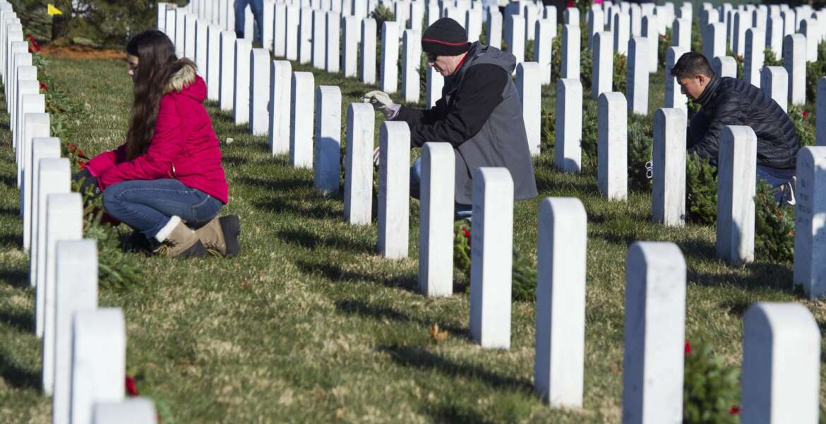 Volunteers place wreaths at headstones in Arlington National Cemetery as Wreaths Across America places remembrance wreaths on the nearly 245,000 headstones at the cemetery in Arlington, Va., Saturday, Dec. 16, 2017. (AP Photo/Cliff Owen)