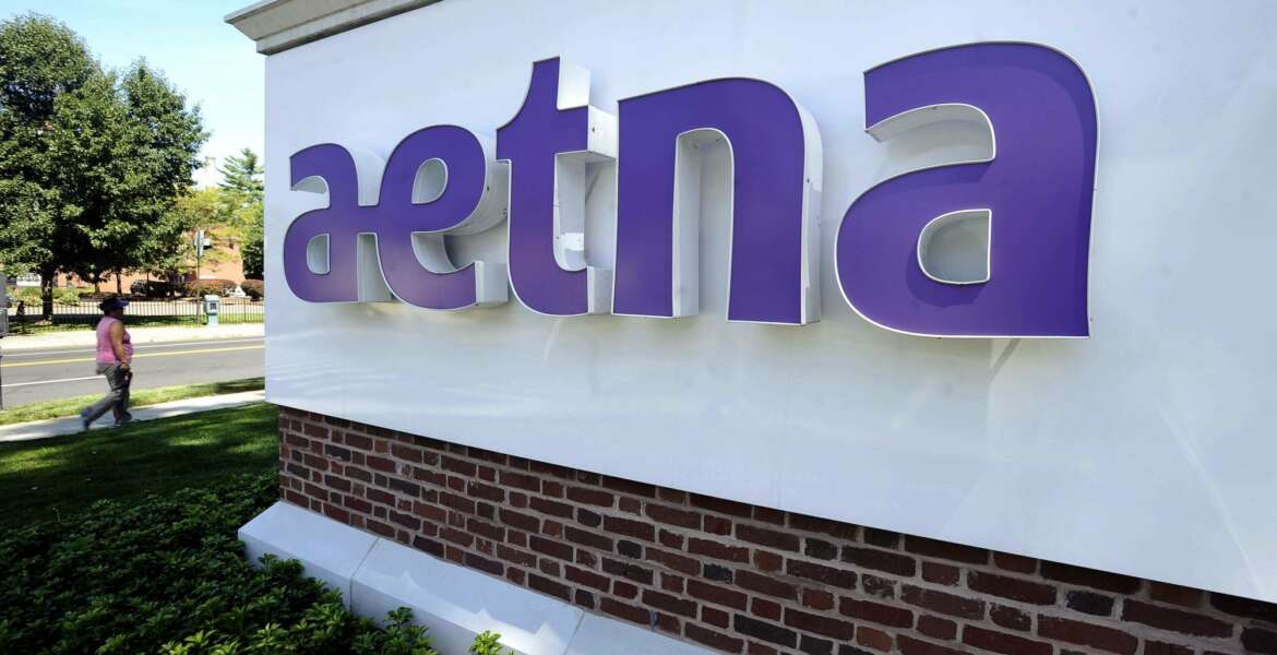 FILE - In this Aug. 19, 2014, file photo, a pedestrian walks by a sign at Aetna headquarters in Hartford, Conn. CVS Health, the second-largest U.S. drugstore chain, is buying Aetna, the third-largest health insurer. The evolution won't happen overnight, but in time, shoppers may find more clinics in CVS stores and more services they can receive through the network of nearly 10,000 locations that the company has built. (AP Photo/Jessica Hill, File)