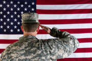 Male Veteran soldier, back to camera, saluting United States of America flag.