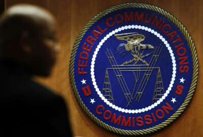 This Thursday, Dec. 14, 2017, photo, shows the seal of the Federal Communications Commission before a meeting in Washington. On Thursday, Dec. 21, 2017, the FCC proposed a $13.4 million fine on TV-station owner Sinclair for not identifying paid programming as advertising. (AP Photo/Jacquelyn Martin)
