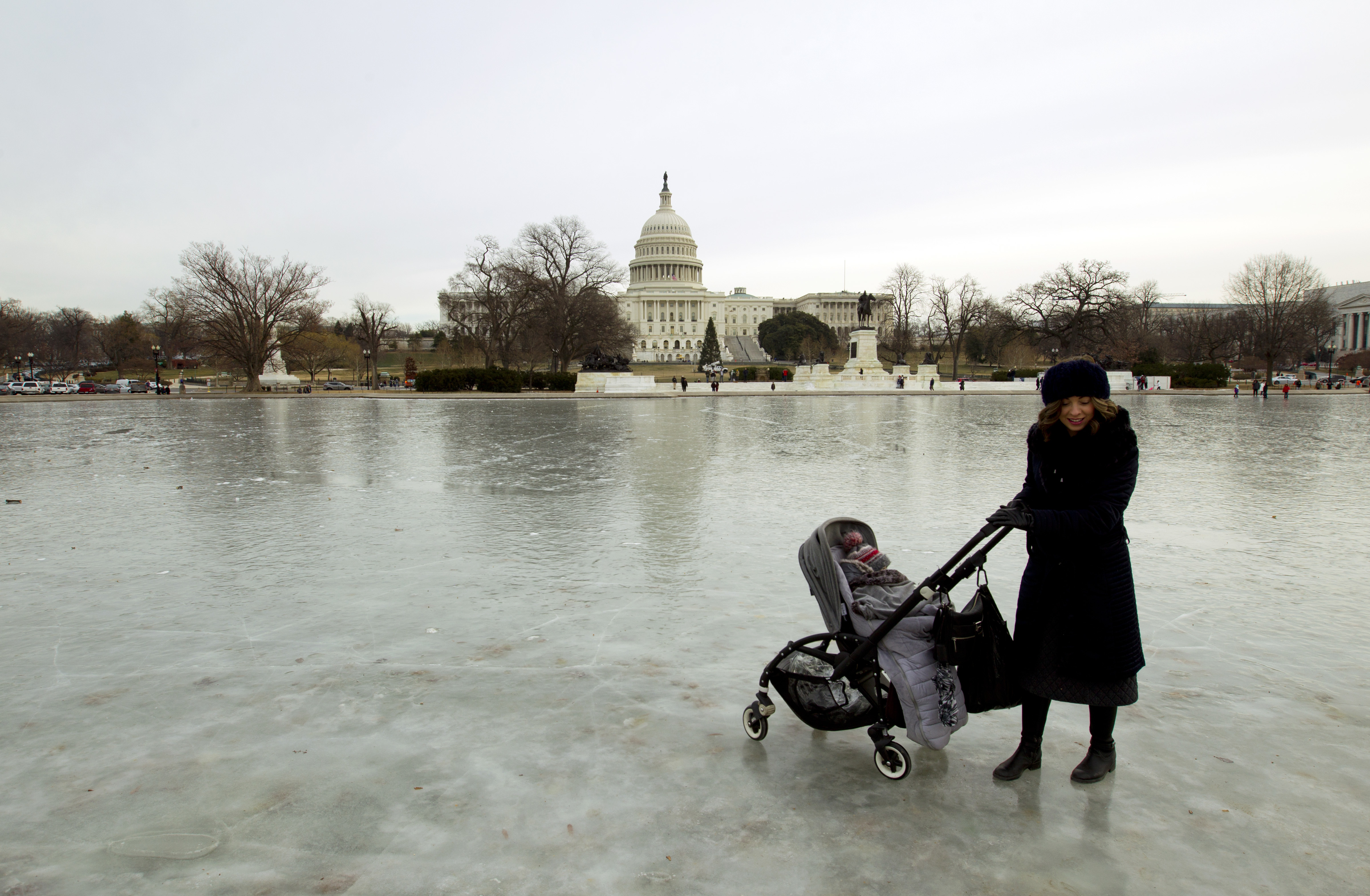 A visitor push her stroller on the frozen reflecting pool, outside of the U.S. Capitol, Wednesday, Jan. 3, 2018, in Washington. Forecasters warned that conditions could worsen, especially in the Northeast. ( AP Photo/Jose Luis Magana)