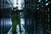 In Data Center Two Military Men Work with Open Server Rack Cabinet. One Holds Military Edition Laptop.