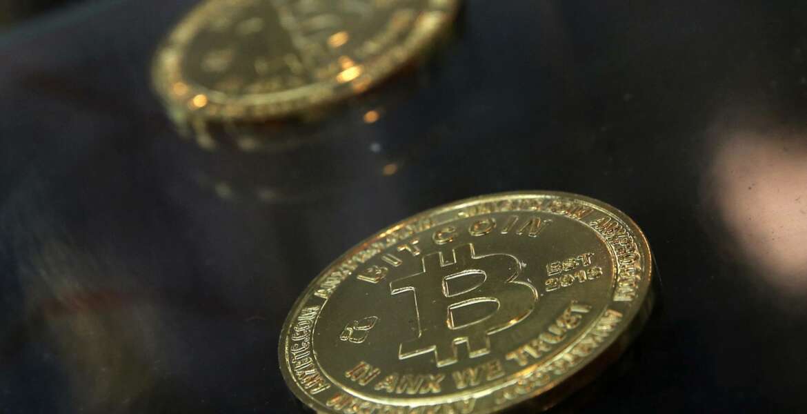 FILE- In this Dec. 8, 2017, file photo, coins are displayed next to a Bitcoin ATM in Hong Kong. The IRS says that cryptocurrency transactions are taxable by law. That means people who made money (or lost it) on Bitcoin trades, “mined” Ethereum or even bought a cup of coffee with digital currency face potential tax implications. Failure to report it could mean potential audits, fines and penalties. (AP Photo/Kin Cheung, File)
