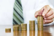 Businessman hand holding coin dollar on money coin stack arranged as a graph on wooden table, concept of money growth and saving money