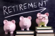 Three pink piggy banks standing on books next to a blackboard with retirement savings message.  Sharp focus on the piggy banks.  Alternative file shown below: