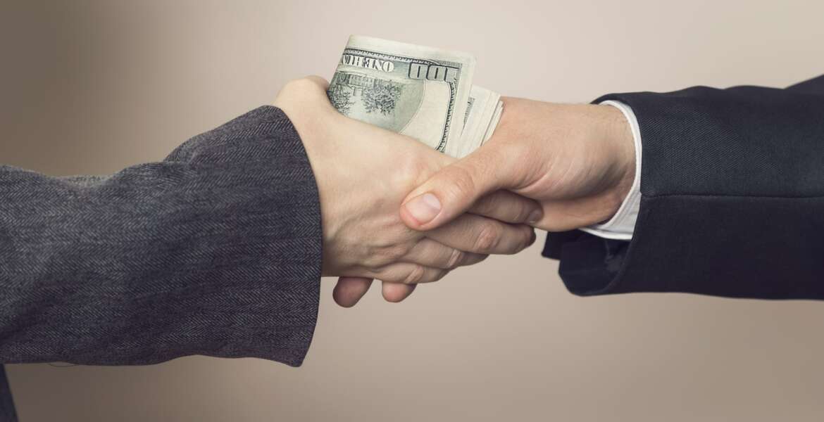 Detail of two business people sealing the deal with bribe money. Selective focus