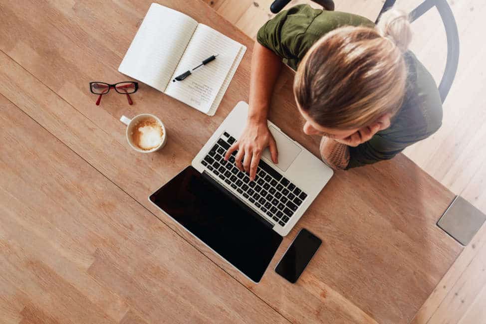 Top view of woman using laptop while sitting at cafe table with laptop, mobile phone, diary, coffee cup and glasses. Female surfing internet at coffee shop.