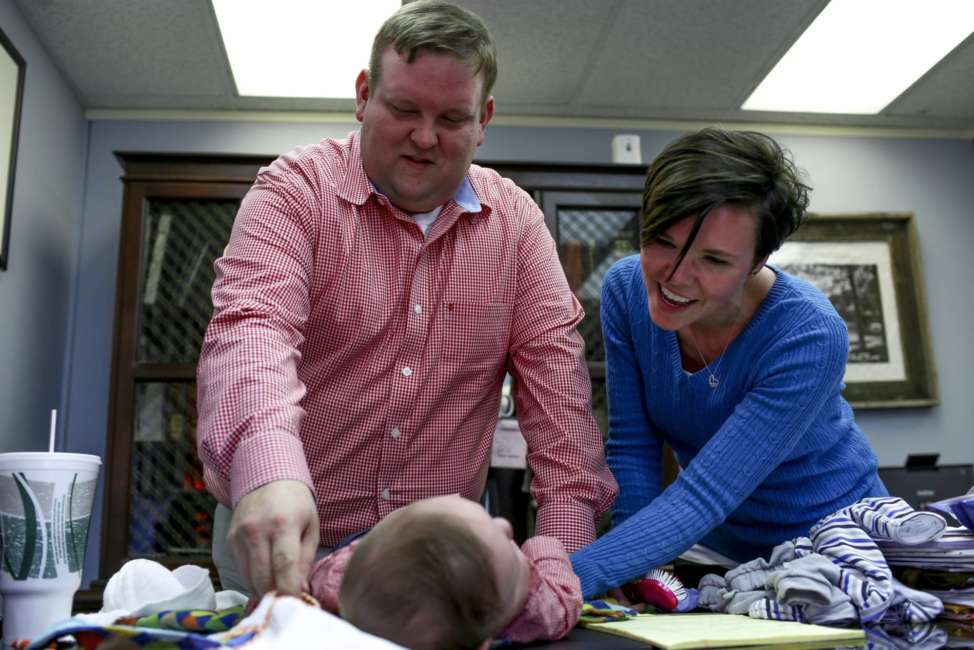 In this March 23, 2018 photo, Philip Ellison and his wife, Katherine Ellison, change their son Patton's clothing at the end of the work day at Philip Ellison's firm Outside Legal Counsel in Hemlock, Mich. If you were born in Michigan in July 1984 or later, you may be among more than five million people whose blood is being held by the state of Michigan, some of which may be used in medical research. A federal lawsuit, filed by Saginaw County Attorney Ellison on behalf of a group of Michigan parents, argues that the practice is unconstitutional and there are no protections in place to stop police or others from accessing the information that can be derived from stored blood samples. (Henry Taylor/The Flint Journal-MLive.com via AP)