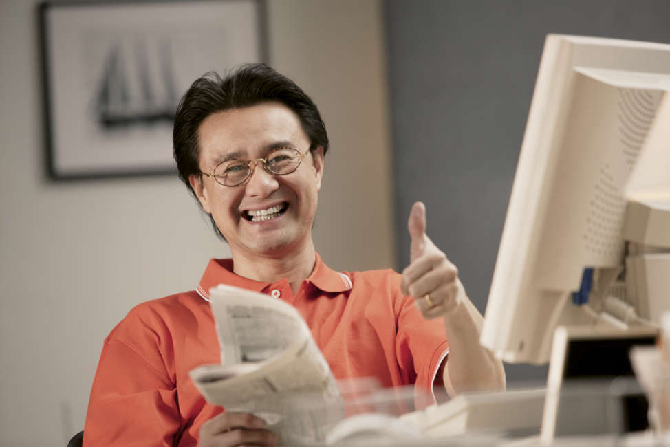 Man at computer holding newspaper