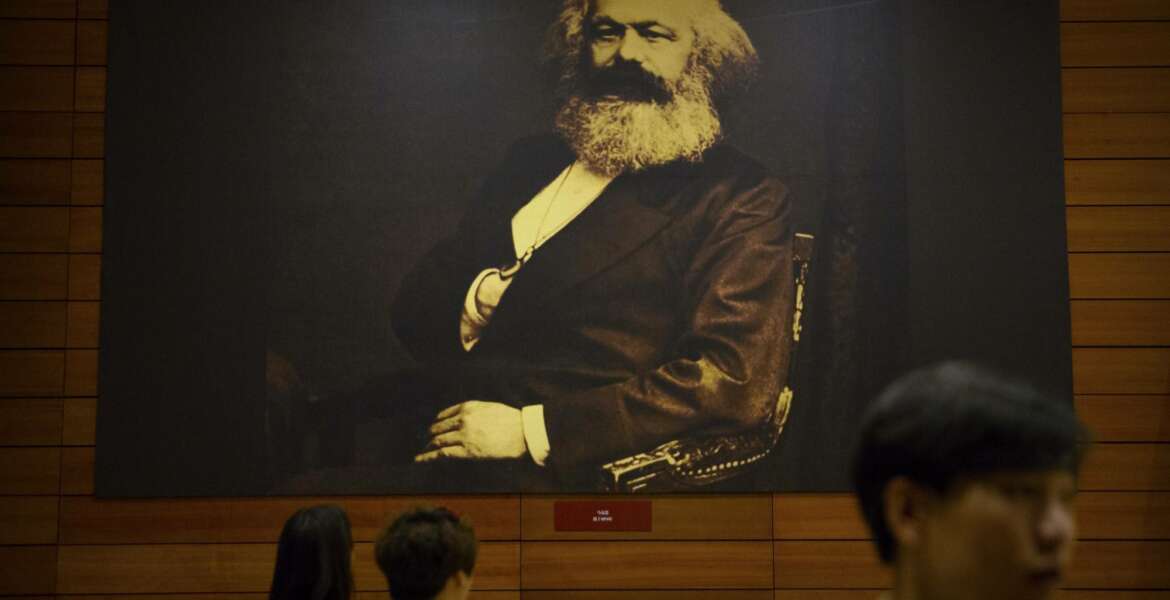 Visitors walk past a photograph of Karl Marx at an exhibition to commemorate the 200th anniversary of his birth at the National Museum in Beijing, Saturday, May 5, 2018. Abroad, China's President Xi Jinping portrays himself as a robust defender of free markets, yet at home, he's leading a campaign to promote the works of communist philosopher Karl Marx, who famously warned of the dangers of global capitalism. (AP Photo/Mark Schiefelbein)