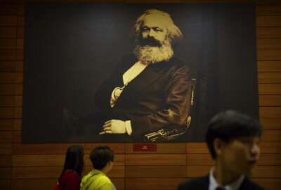 Visitors walk past a photograph of Karl Marx at an exhibition to commemorate the 200th anniversary of his birth at the National Museum in Beijing, Saturday, May 5, 2018. Abroad, China's President Xi Jinping portrays himself as a robust defender of free markets, yet at home, he's leading a campaign to promote the works of communist philosopher Karl Marx, who famously warned of the dangers of global capitalism. (AP Photo/Mark Schiefelbein)
