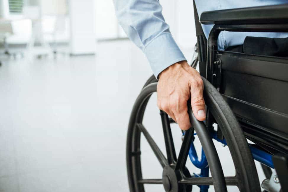 Businessman in wheelchair, hand on wheel close up, office interior on background