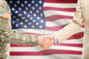 USA military man in uniform and civil man in suit shaking hands with national flag on background - United States