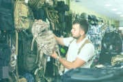 positive spanish  man choosing textile backpack gun in military shop