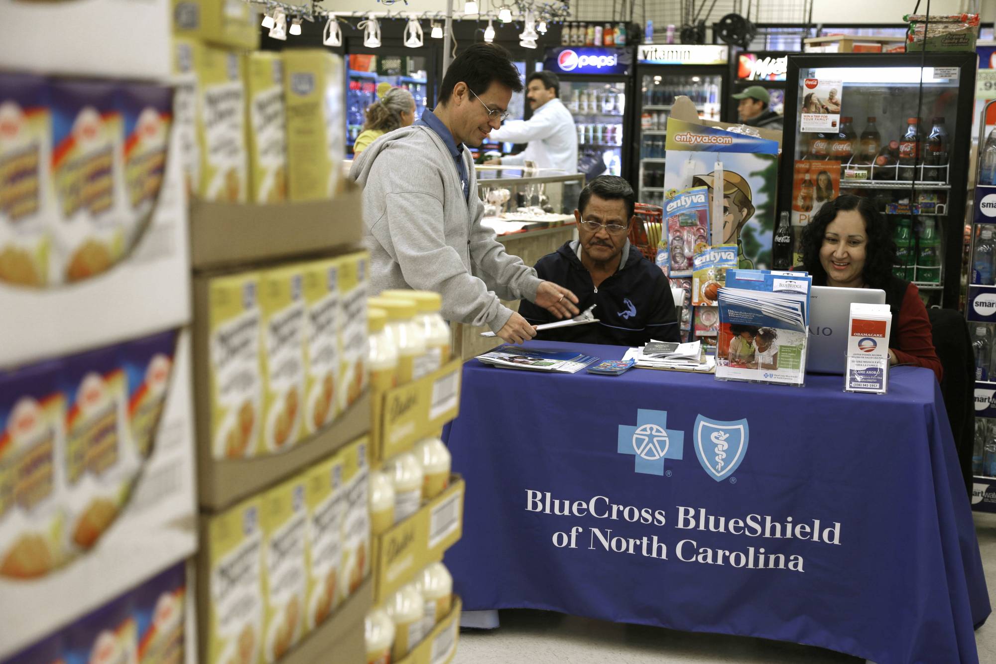 FILE - In this file photo taken Nov. 22, 2014, Blue Bridge Benefits LLC agent Patricia Sarabia, right, and Adolfo Briceno, left, with Spanish Speaking LLC, help a potential customer with Blue Cross Blue Shield at a kiosk promoting Obama Care at Compare Foods in Winston-Salem, N.C. A new poll finds that more than half of Hispanic adults have encountered a communication barrier in the health care system. (AP Photo/Gerry Broome, file)