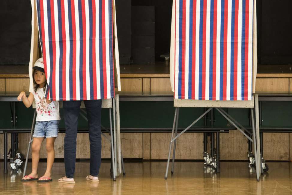 Paige Arasaki, 6, peeks out from a voting booth occupied by her mother, Kathy, at the Aiea High School polling station on Saturday, Aug. 11, 2018, in Aiea,  Hawaii.  The winners of most of the Democratic Party's primary races in Hawaii this weekend will be the favorites to win the general election in November. The most hotly contested matches in this deep blue state on Saturday are for governor and the state's 1st Congressional District.  (Cindy Ellen Russell /Honolulu Star-Advertiser via AP)