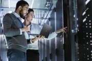 Male IT Specialist Holds Laptop and Discusses Work with Female Server Technician. They're Standing in Data Center, Rack Server Cabinet is Open.