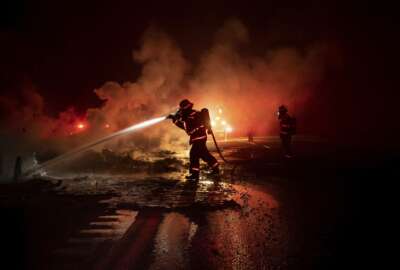 A firefighter sprays the smoldering remains of a vehicle on Interstate 5 as the Delta Fire burns in the Shasta-Trinity National Forest, Calif., on Wednesday, Sept. 5, 2018. Parked trucks lined more than two miles of the highway as both directions remained closed to traffic. (AP Photo/Noah Berger)