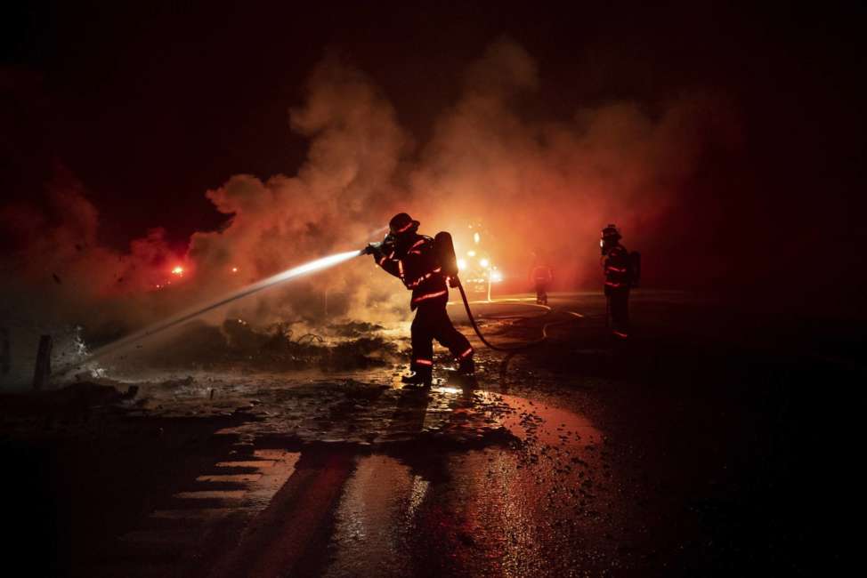 A firefighter sprays the smoldering remains of a vehicle on Interstate 5 as the Delta Fire burns in the Shasta-Trinity National Forest, Calif., on Wednesday, Sept. 5, 2018. Parked trucks lined more than two miles of the highway as both directions remained closed to traffic. (AP Photo/Noah Berger)