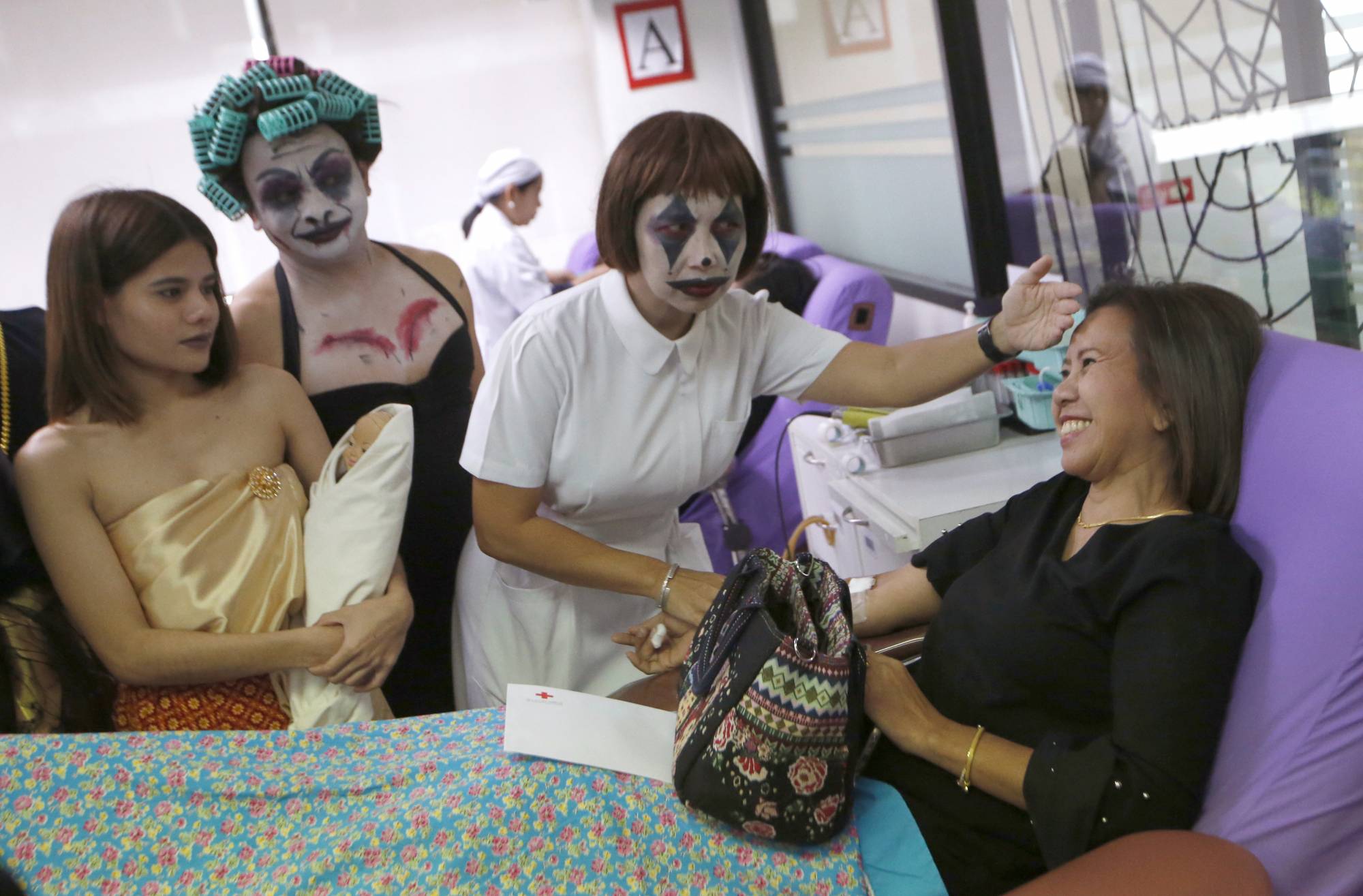 Thanat Chotrat, second from left, and Manful Bumroongton, third from left, dressed in a ghost costume for Halloween talk to volunteer donate blood on bed at the Thai Red Cross in Bangkok, Thailand, Thailand, Wednesday, Oct. 31, 2018. (AP Photo/Sakchai Lalit)