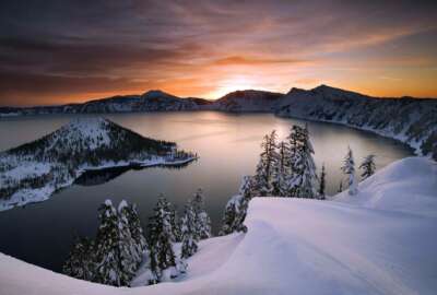FILE - In this January 2006 file photo, the sun rises over Crater Lake, Ore. Access to Crater Lake and other national parks will be limited due to the government shutdown. (Marc Adamus/The Register-Guard via AP, File)