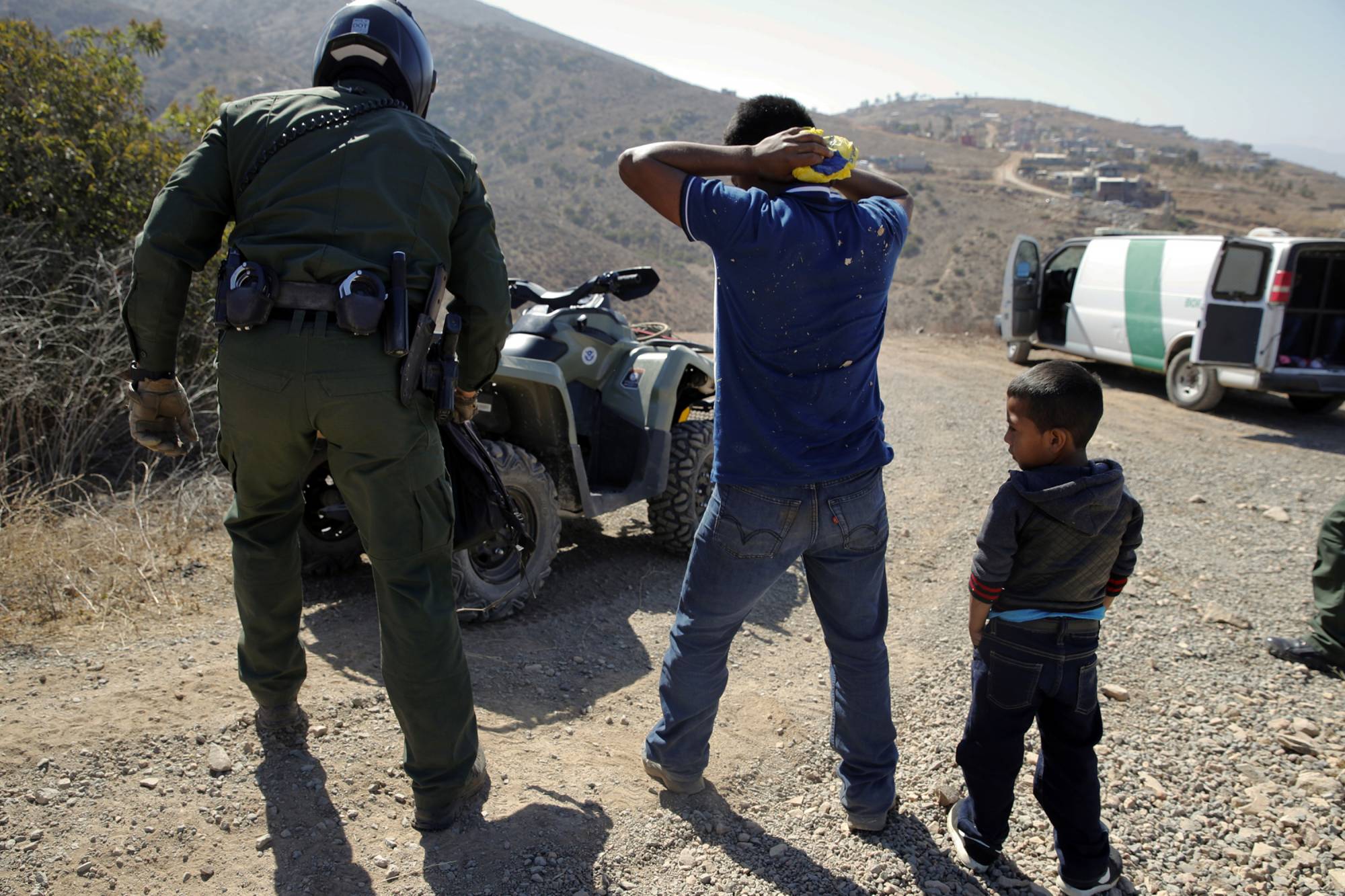 FILE - In this June 28, 2018, file photo, a Guatemalan father and son, who crossed the U.S.-Mexico border illegally, are apprehended by a U.S. Border Patrol agent in San Diego. Children torn from their parents, refugees turned away, tear gas fired on asylum-seekers, and a swath of the globe derided by the president in crude language. In a breathless 2018, they were just a handful of headlines on immigration, one of the year’s most dominant issues. (AP Photo/Jae C. Hong, File)
