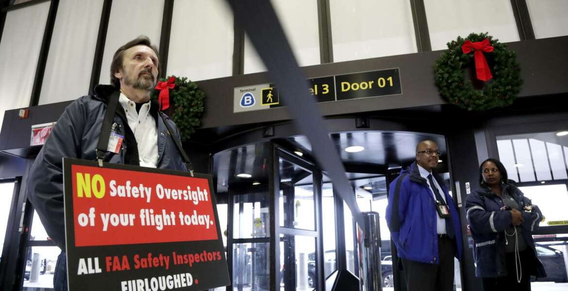 FILE - In this Tuesday, Jan. 8, 2019, file photo, Federal Aviation Administration employee Michael Jessie, who is currently working without pay as an aviation safety inspector for New York international field office overseeing foreign air carriers, holds a sign while attending a news conference at Newark Liberty International Airport in Newark, N.J. The FAA says it is calling 2,200 safety inspectors back to work by the end of this week. The inspectors certify work done by airlines, aircraft manufacturers and repair shops.  (AP Photo/Julio Cortez, File)